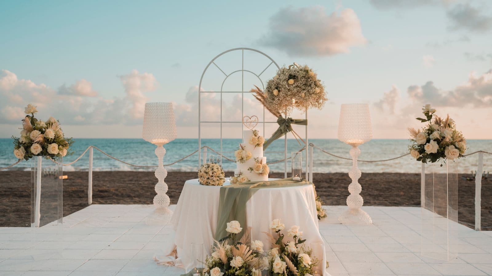 Wedding reception table with floral arrangements and cake set on an oceanfront terrace at dusk