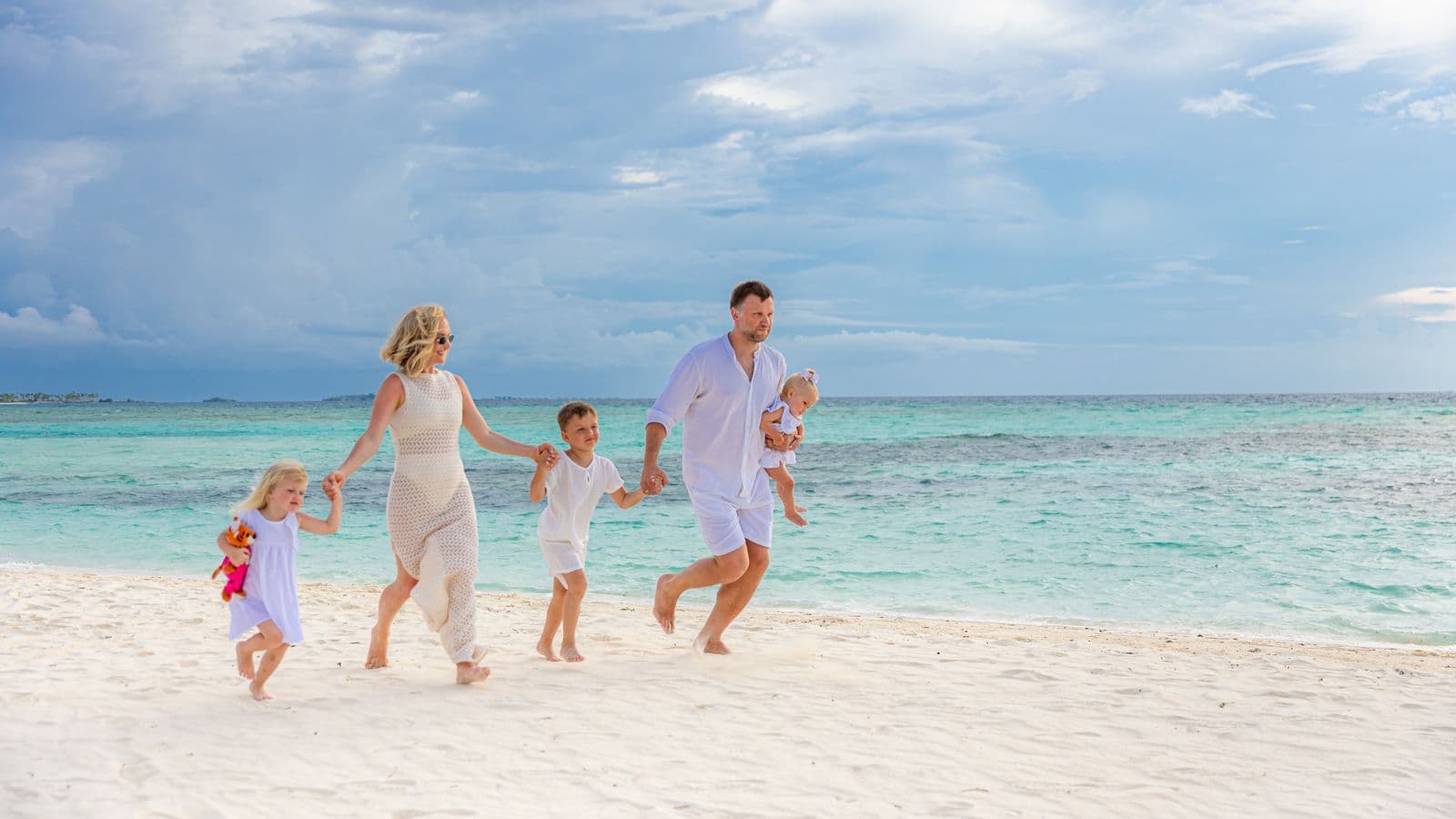 Family of five walking hand in hand on a white-sand beach