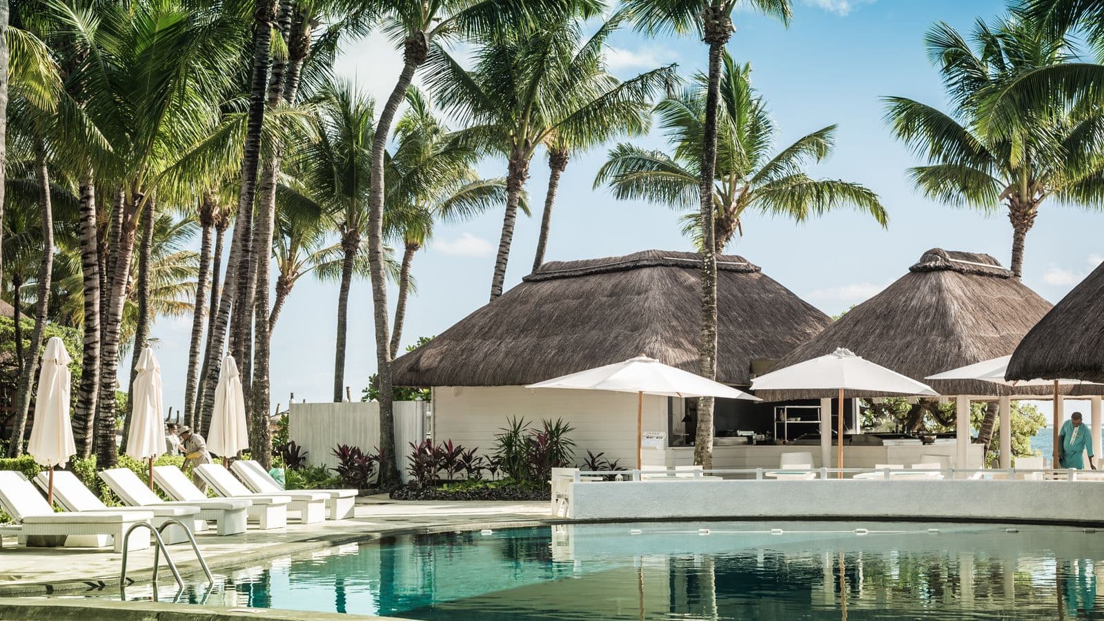 All-inclusive resort pool with thatched-roof swim-up bar and palm trees