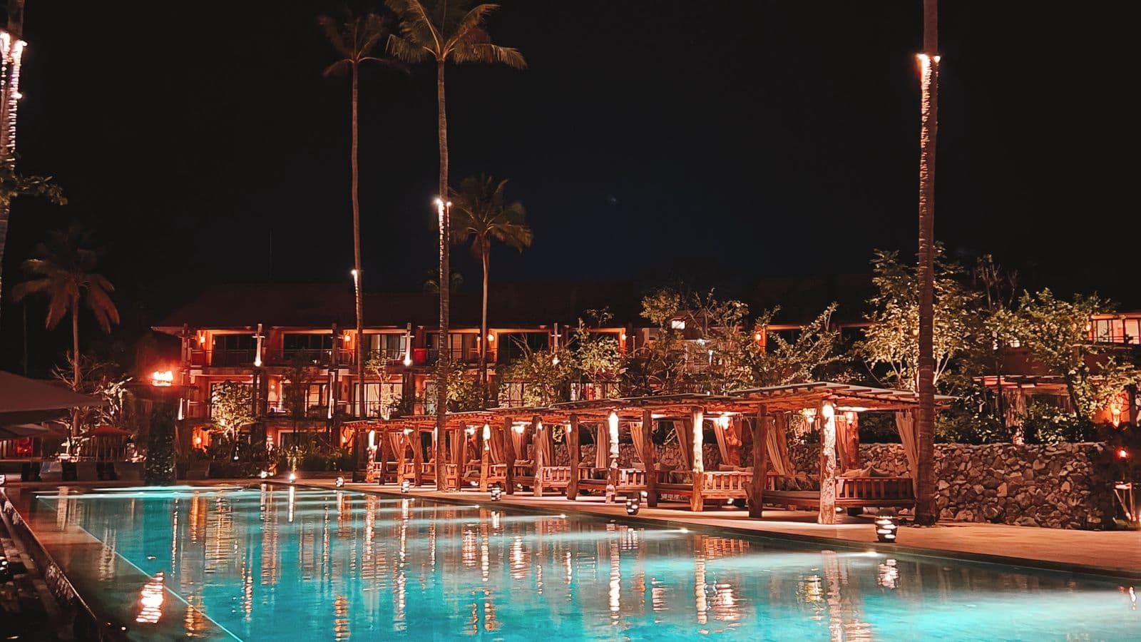 Adults-only resort pool lit at night with cabanas and palm trees