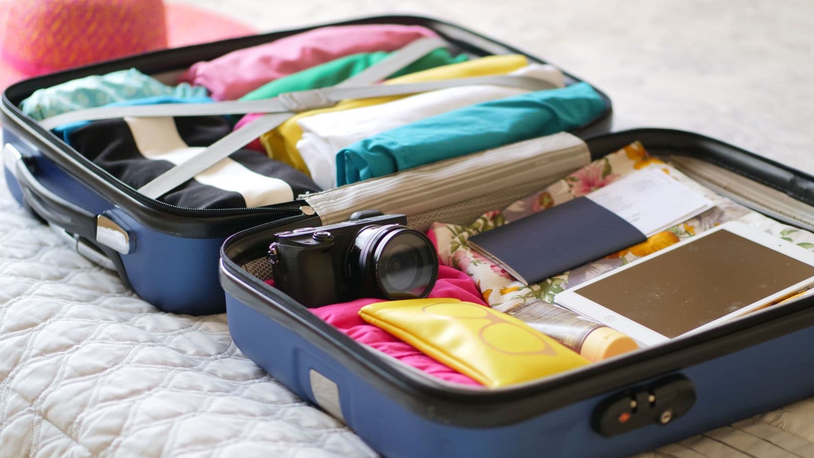 Open suitcase packed for a trip with passport and travel documents on a bed