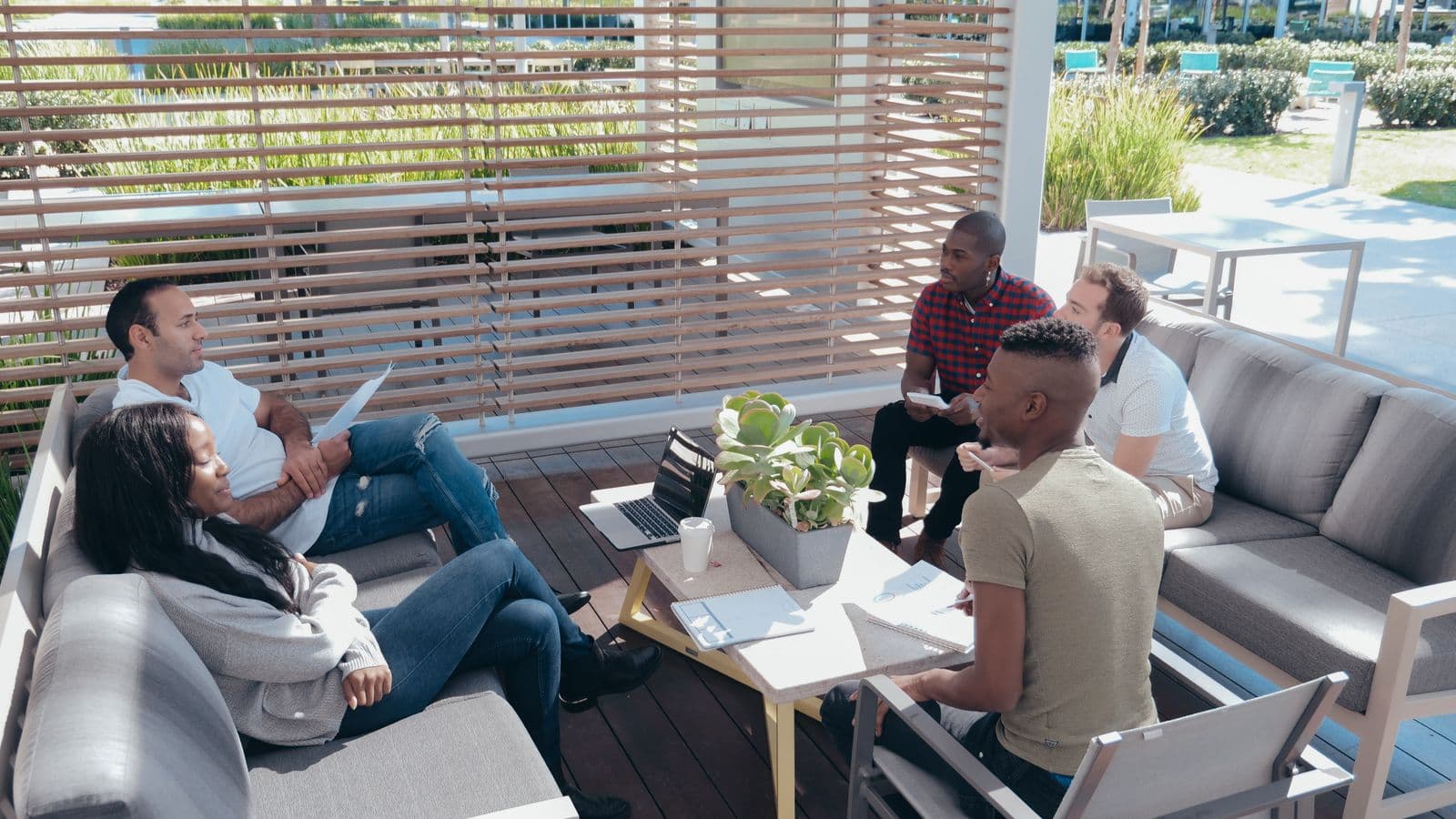 Distributed team working together in outdoor lounge seating with laptops and notes, illustrating a remote company gathering in person