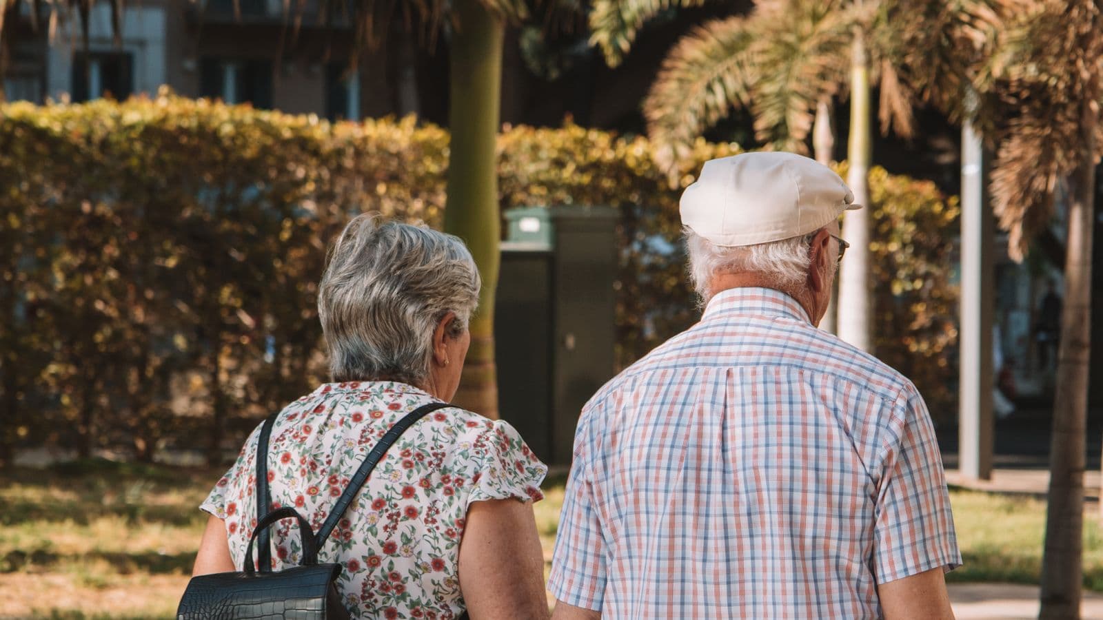 Senior couple walking together on a sunlit palm-lined promenade in Málaga, Spain